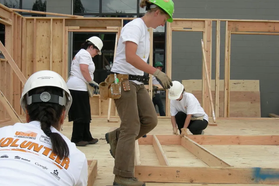 Habitat for Humanity volunteers in construction helmets buildign a wood-frame house.